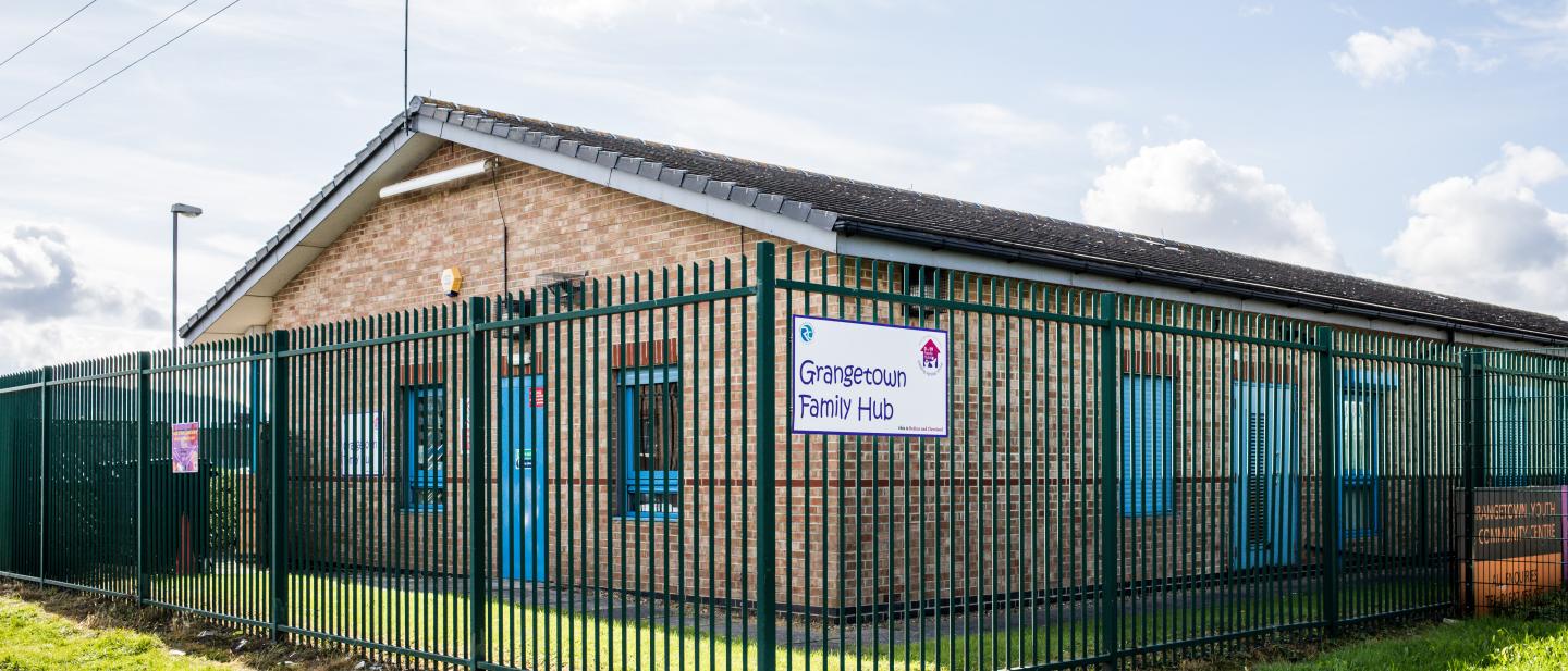 Picture of a ne floor building surrounded by green grass and a fence with a sign reading "Grangetown Family Hub""