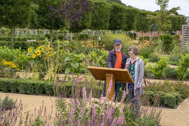 A man and a woman reading a display sign within the gardens surrounded by plants and trees 